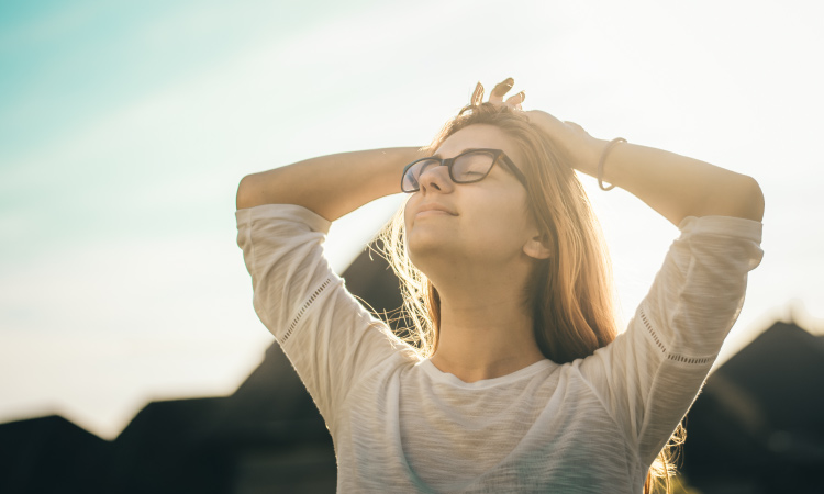 Blonde woman wearing glasses outside by mountains breathes in deeply as she thinks about an anxiety-free visit to the dentist