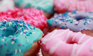 Closeup of a cluster of donuts with pink, blue, and purple icing with sprinkles and sugar that increase your risk of cavities