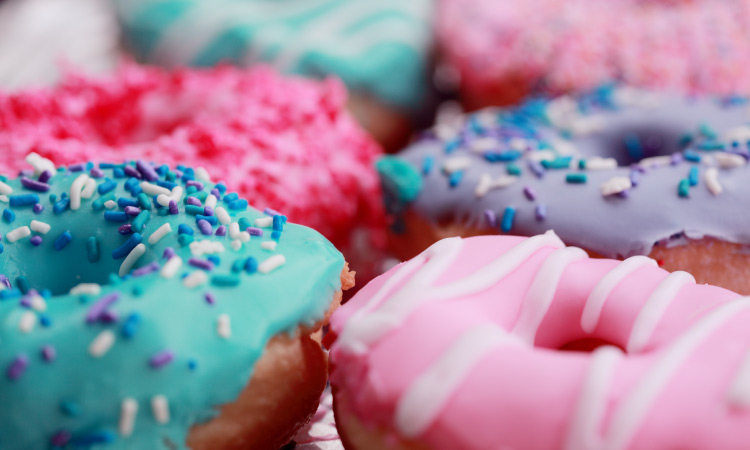 A cluster of donuts with pink, blue, and purple icing with sprinkles and sugar that increase the risk of cavities